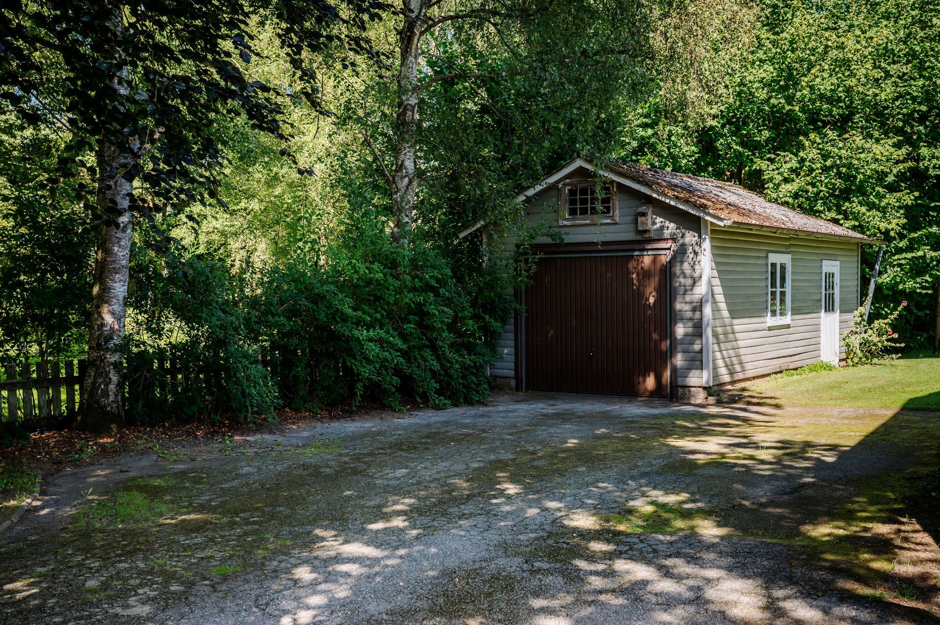 Rymlig gårdsplan innanför grindarna med plats för flera fordon framför garaget.