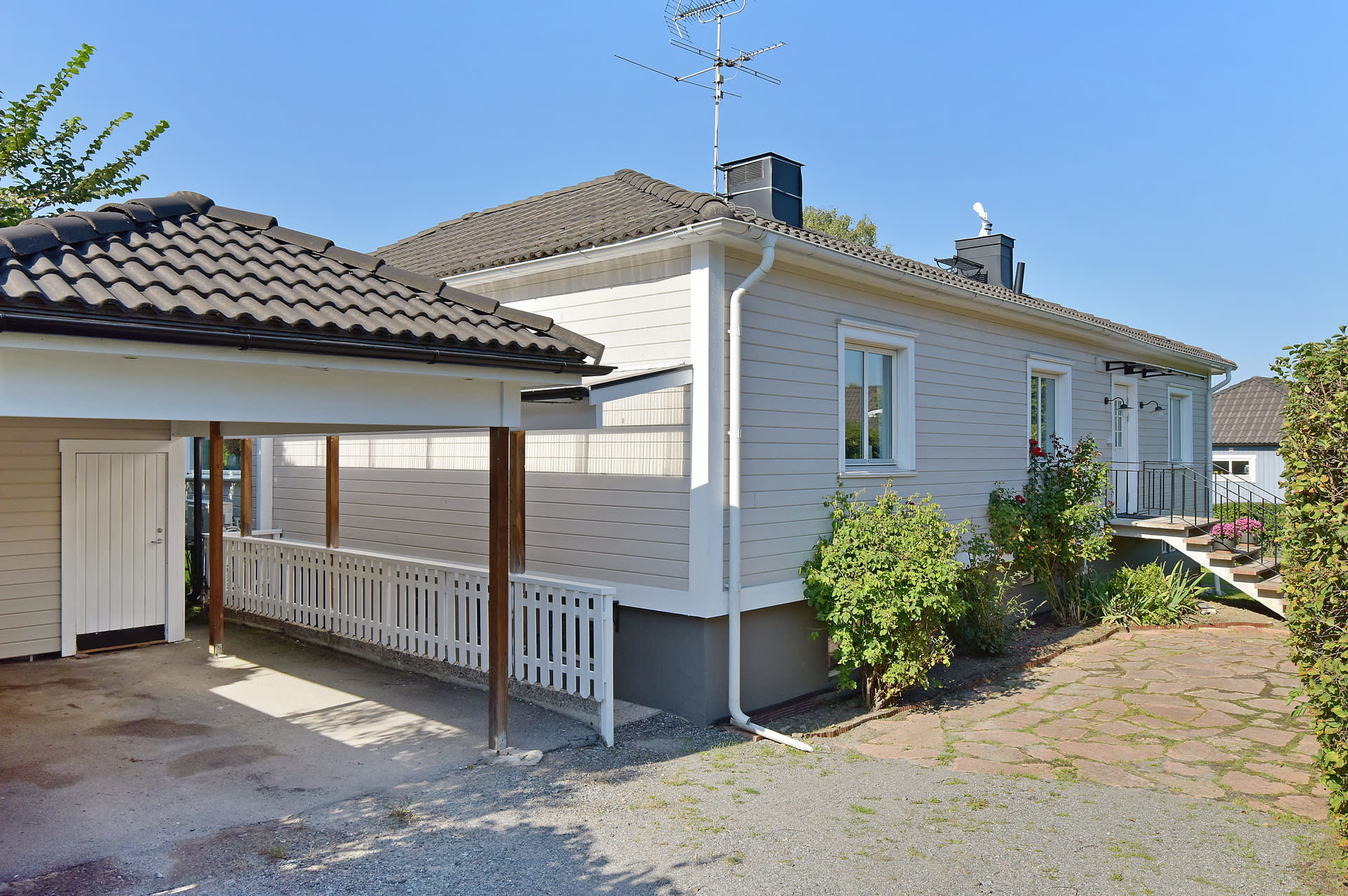 Carport med förrådsdel. Staket skyddar mot trappa med dörr till det fina källarplanet